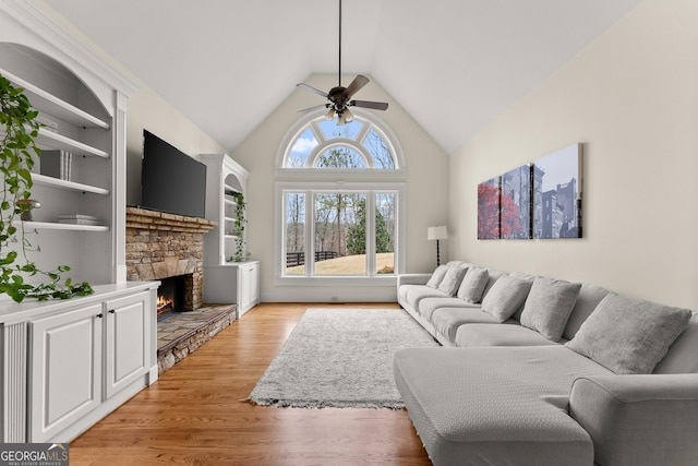 living area featuring built in shelves, light wood finished floors, high vaulted ceiling, a fireplace, and ceiling fan