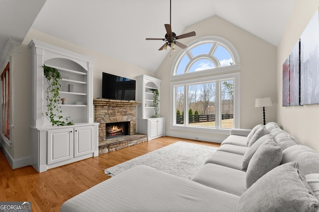 living area with built in shelves, a ceiling fan, high vaulted ceiling, a stone fireplace, and light wood-style floors