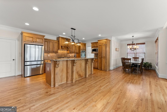 kitchen featuring a kitchen bar, brown cabinets, stainless steel appliances, an inviting chandelier, and light stone countertops