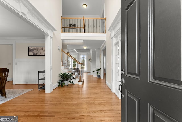 entryway featuring ornamental molding, a high ceiling, light wood finished floors, decorative columns, and stairs