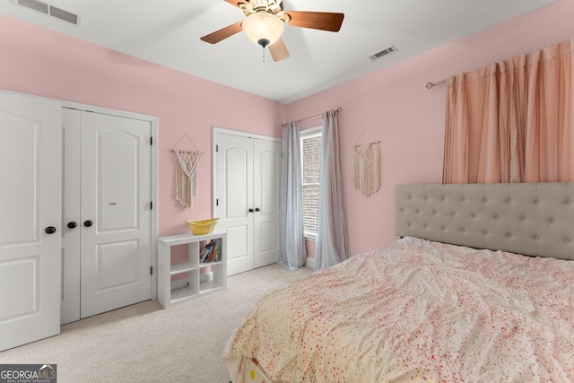carpeted bedroom featuring a ceiling fan, visible vents, and multiple closets