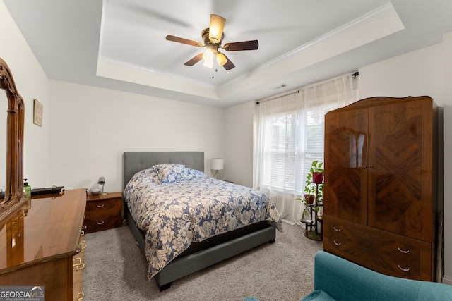 carpeted bedroom featuring a tray ceiling, a ceiling fan, visible vents, and ornamental molding