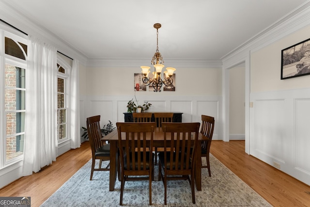 dining area featuring an inviting chandelier, a decorative wall, crown molding, and light wood-type flooring