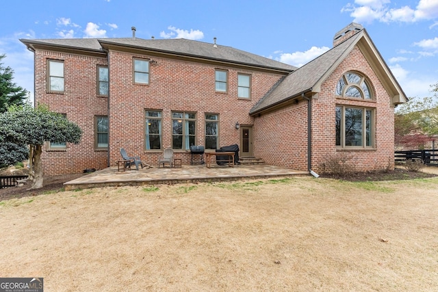 rear view of property featuring brick siding, a chimney, and a patio area
