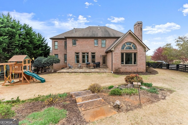 rear view of property with a playground, fence, brick siding, and a chimney