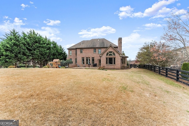 back of property featuring fence, a chimney, a playground, a lawn, and brick siding