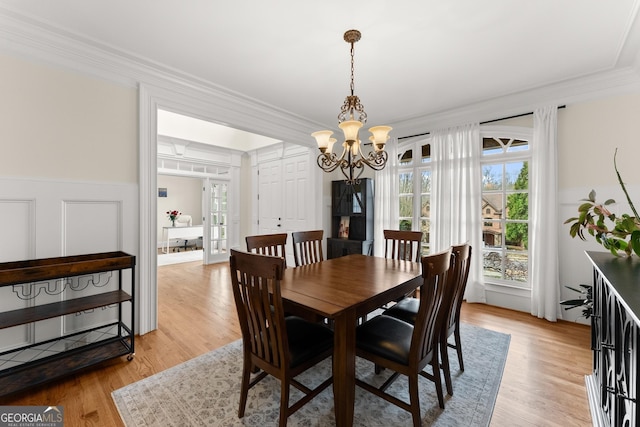 dining area featuring a wainscoted wall, an inviting chandelier, light wood-style flooring, ornamental molding, and a decorative wall