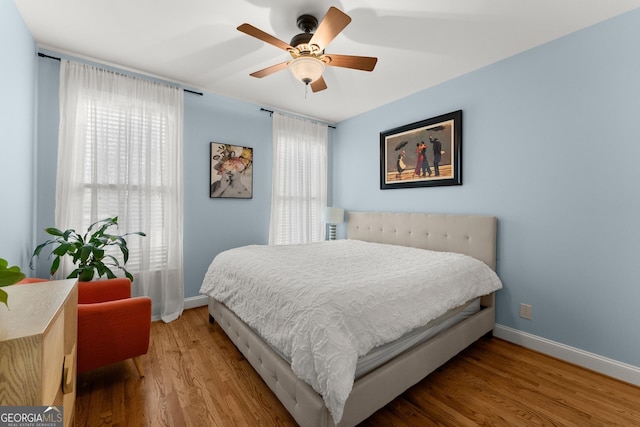 bedroom featuring ceiling fan, baseboards, multiple windows, and wood finished floors