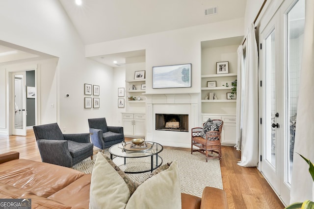 living area with visible vents, light wood-style flooring, a high end fireplace, built in shelves, and vaulted ceiling