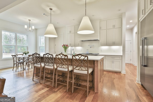 kitchen with light countertops, light wood-style flooring, visible vents, stainless steel appliances, and an island with sink