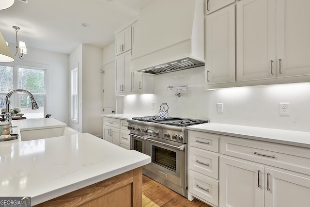 kitchen with light countertops, light wood-style flooring, a sink, range with two ovens, and custom exhaust hood
