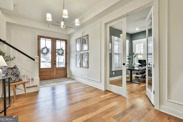 foyer entrance with stairs, a notable chandelier, light wood-style floors, and french doors