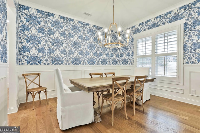 dining space featuring a wainscoted wall, wood finished floors, visible vents, wallpapered walls, and an inviting chandelier