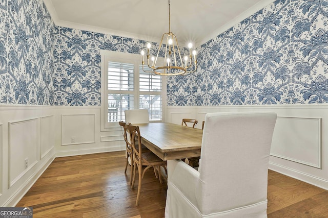 dining room with a wainscoted wall, a notable chandelier, wood finished floors, wallpapered walls, and ornamental molding