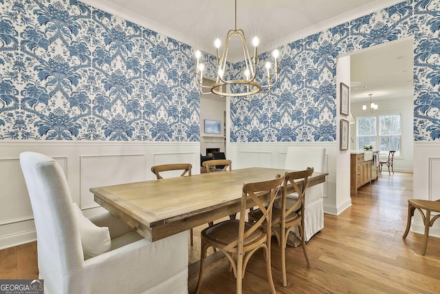 dining area featuring light wood-style flooring, wallpapered walls, a chandelier, and wainscoting
