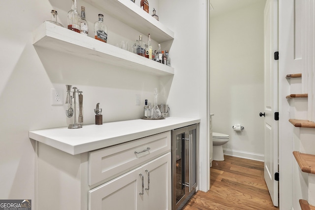 bathroom with baseboards, toilet, wine cooler, wood finished floors, and vanity