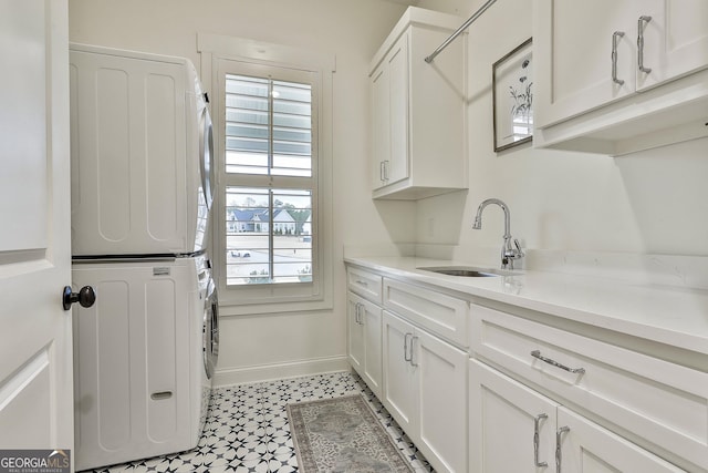 clothes washing area with a sink, light floors, stacked washer and clothes dryer, baseboards, and cabinet space