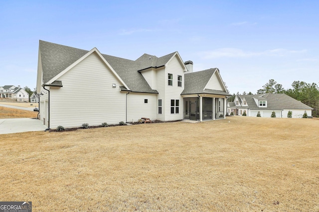 back of house with a lawn, a sunroom, roof with shingles, and a chimney