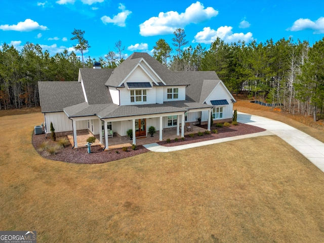 view of front facade with stone siding, concrete driveway, a front yard, roof with shingles, and cooling unit