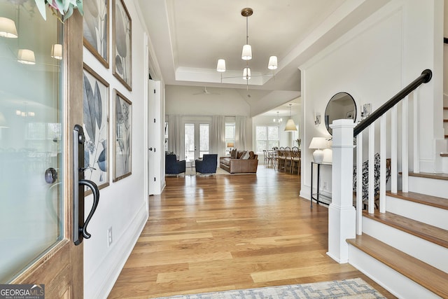 entryway with french doors, a raised ceiling, light wood-style floors, and stairway
