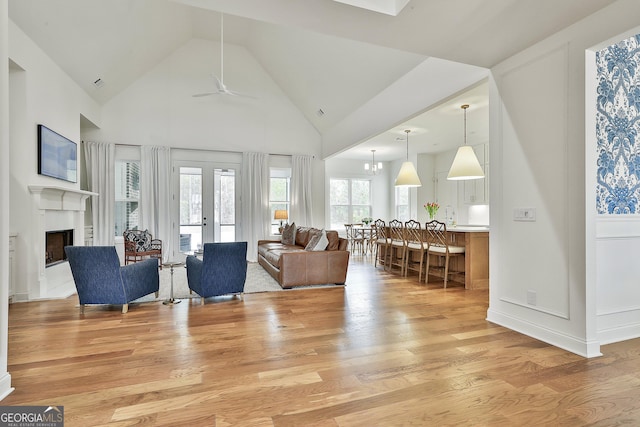 living room featuring french doors, high vaulted ceiling, light wood-style floors, ceiling fan, and a fireplace