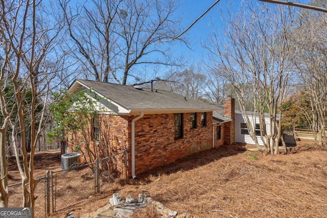 view of side of home featuring brick siding, fence, a chimney, and central AC unit