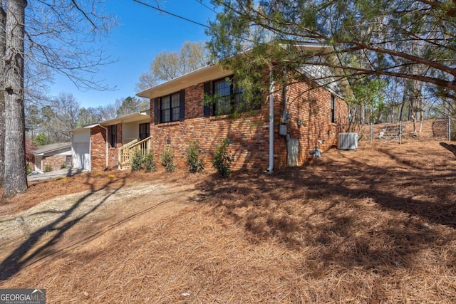 view of front of property featuring an attached garage, fence, central air condition unit, and brick siding