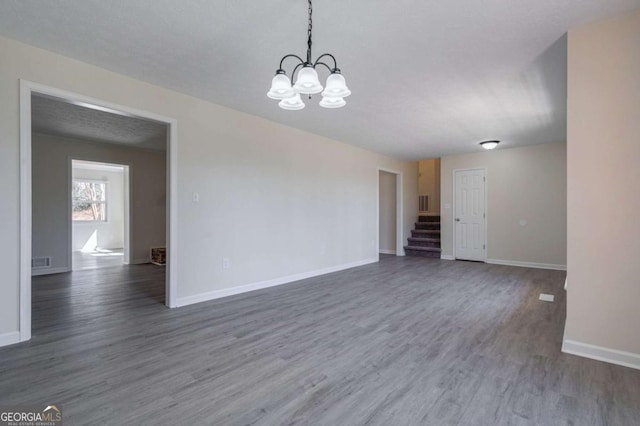 empty room featuring a chandelier, stairs, baseboards, wood finished floors, and visible vents
