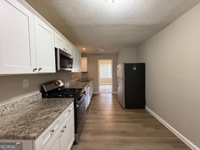 1643 Columbia Dr, Decatur, GA 30032 - kitchen with baseboards, light wood-style flooring, stainless steel appliances, a textured ceiling, and white cabinetry