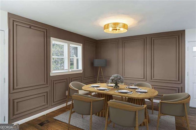 dining space with a decorative wall, visible vents, and dark wood-style flooring
