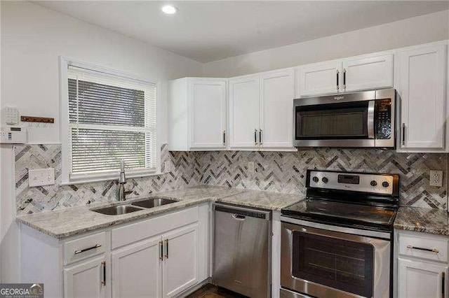 kitchen with light stone countertops, decorative backsplash, appliances with stainless steel finishes, white cabinetry, and a sink