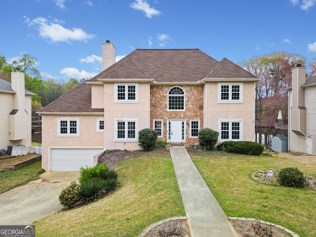 colonial house featuring a front yard, an attached garage, a chimney, concrete driveway, and stucco siding