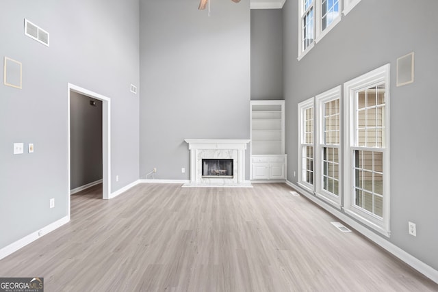 unfurnished living room featuring visible vents, baseboards, ceiling fan, light wood finished floors, and a towering ceiling