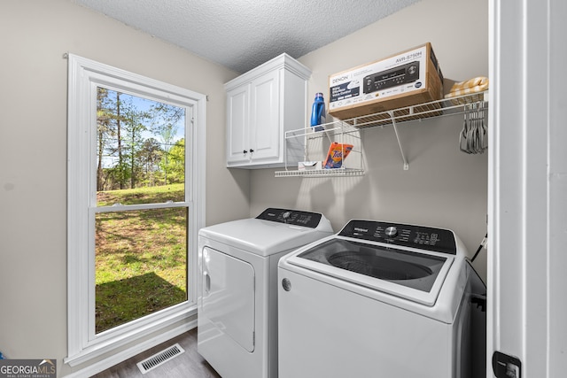 laundry room with a textured ceiling, washing machine and dryer, visible vents, wood finished floors, and cabinet space