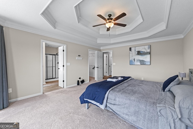 bedroom with a tray ceiling, a ceiling fan, a walk in closet, crown molding, and carpet flooring