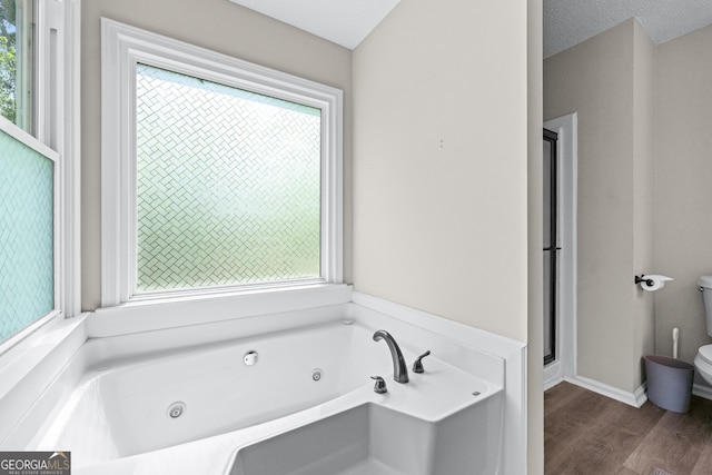 full bath featuring plenty of natural light, wood finished floors, a whirlpool tub, and toilet