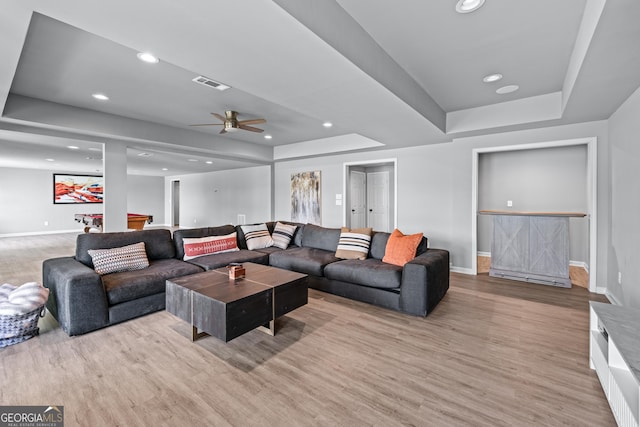 living room featuring light wood finished floors, a raised ceiling, visible vents, a ceiling fan, and baseboards