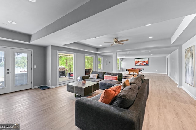 living area with a raised ceiling, light wood-style flooring, baseboards, and french doors