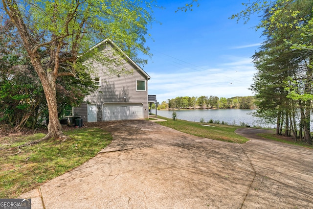 view of property exterior with an attached garage, driveway, a water view, and a yard