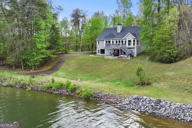 rear view of property with a chimney, a yard, stairs, and a deck with water view