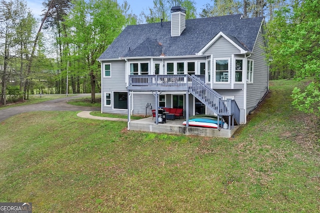 rear view of house featuring a patio area, a lawn, a chimney, a deck, and roof with shingles
