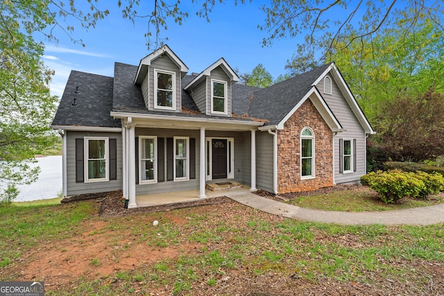 cape cod home with stone siding, a shingled roof, and covered porch