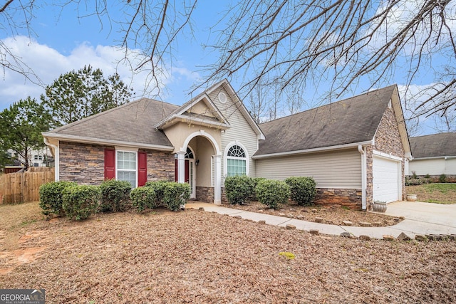 view of front of property with stone siding, fence, concrete driveway, a shingled roof, and a garage