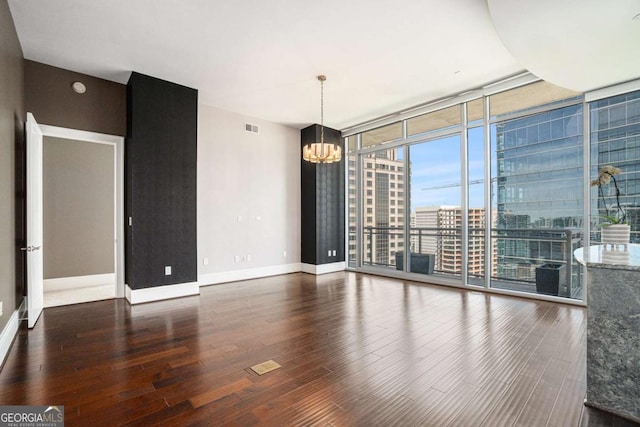 unfurnished room with a wall of windows, wood finished floors, baseboards, a city view, and a notable chandelier