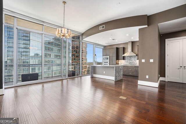 unfurnished living room featuring baseboards, visible vents, an inviting chandelier, dark wood-style flooring, and floor to ceiling windows