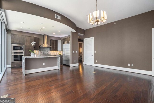 kitchen with visible vents, dark brown cabinets, wall chimney range hood, built in appliances, and a notable chandelier