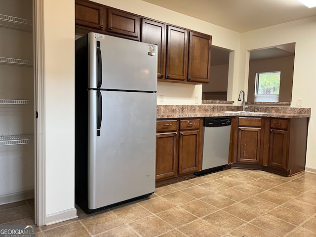 kitchen featuring stainless steel dishwasher, dark brown cabinets, a sink, light countertops, and freestanding refrigerator