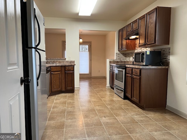 kitchen featuring backsplash, baseboards, stainless steel microwave, freestanding refrigerator, and under cabinet range hood