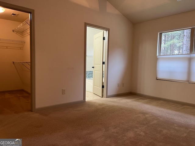 unfurnished bedroom with light colored carpet, baseboards, lofted ceiling, a spacious closet, and visible vents