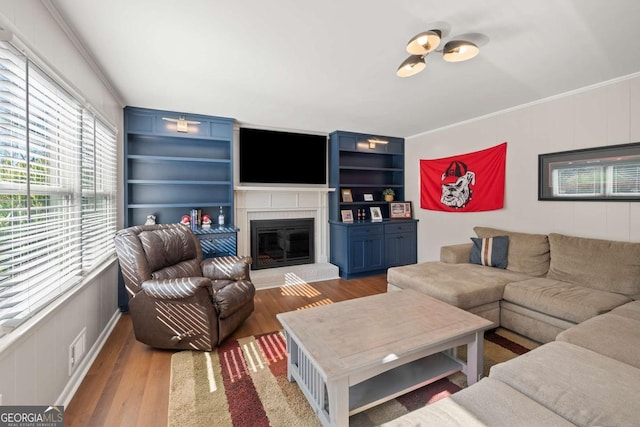 living area with visible vents, built in shelves, wood finished floors, a fireplace, and crown molding